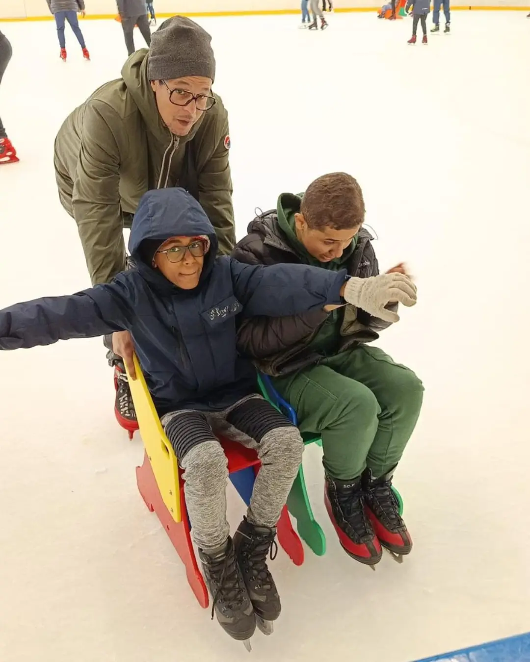 Un encadrant pousse deux enfants assis sur une luge à la patinoire